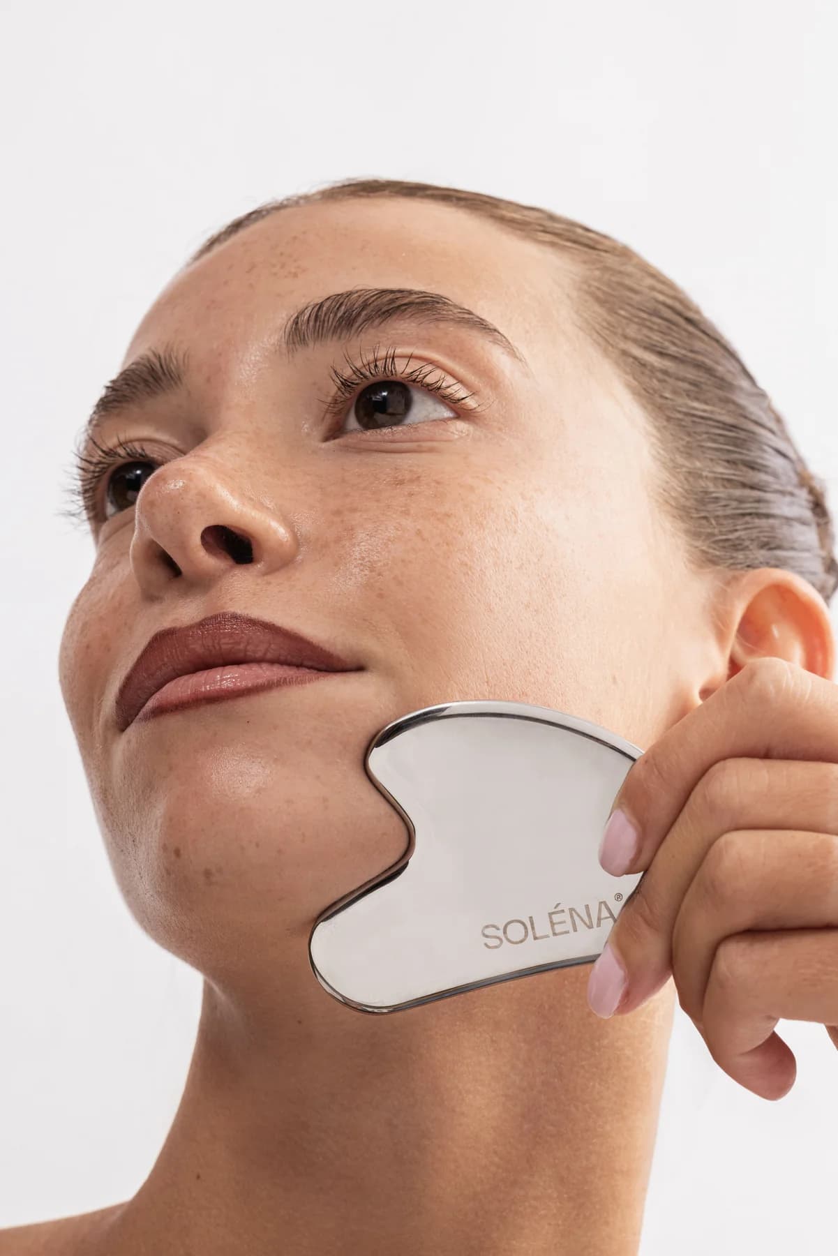SOLÉNA stainless steel Gua Sha held against the cheek